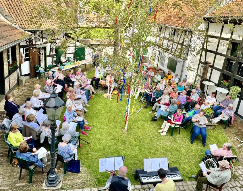 Blick von oben in den Innenhof des Heimatmuseums. Rund um einen Maibaum sitzen Teilnehmende und die Band.