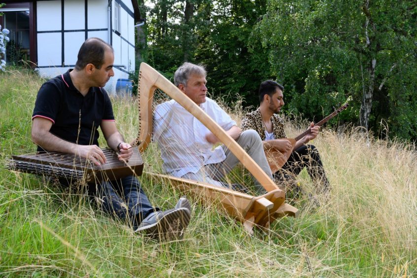 Das Tarab-Trio im hohen Gras sitzend, die Instrumente in der Hand.
